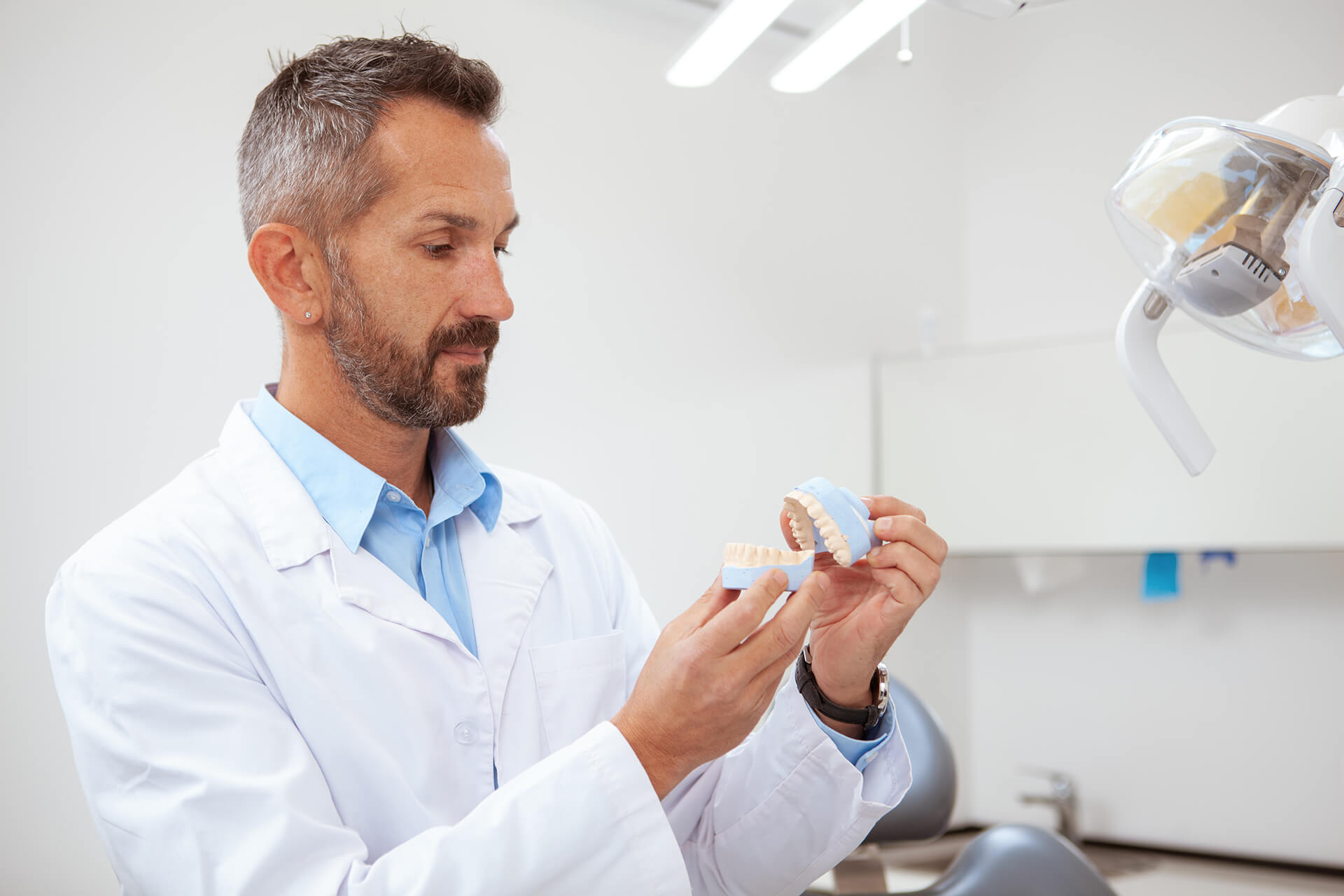 attractive-mature-male-dentist-examining-jaw-mold-working-his-clinic