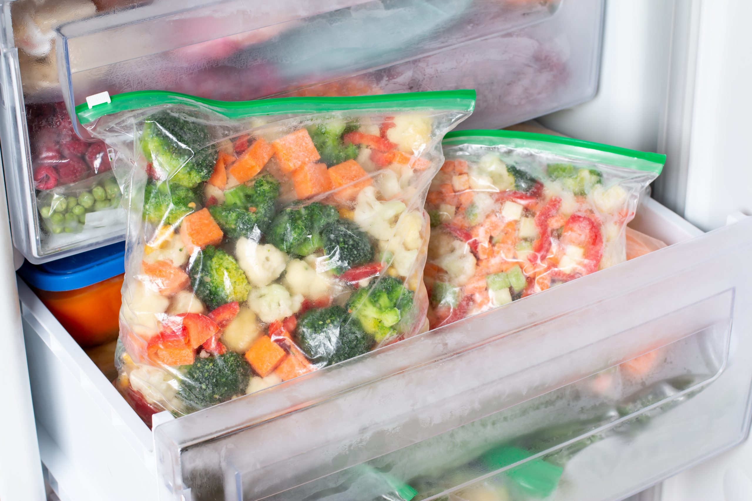 Plastic bags with different frozen vegetables in refrigerator.