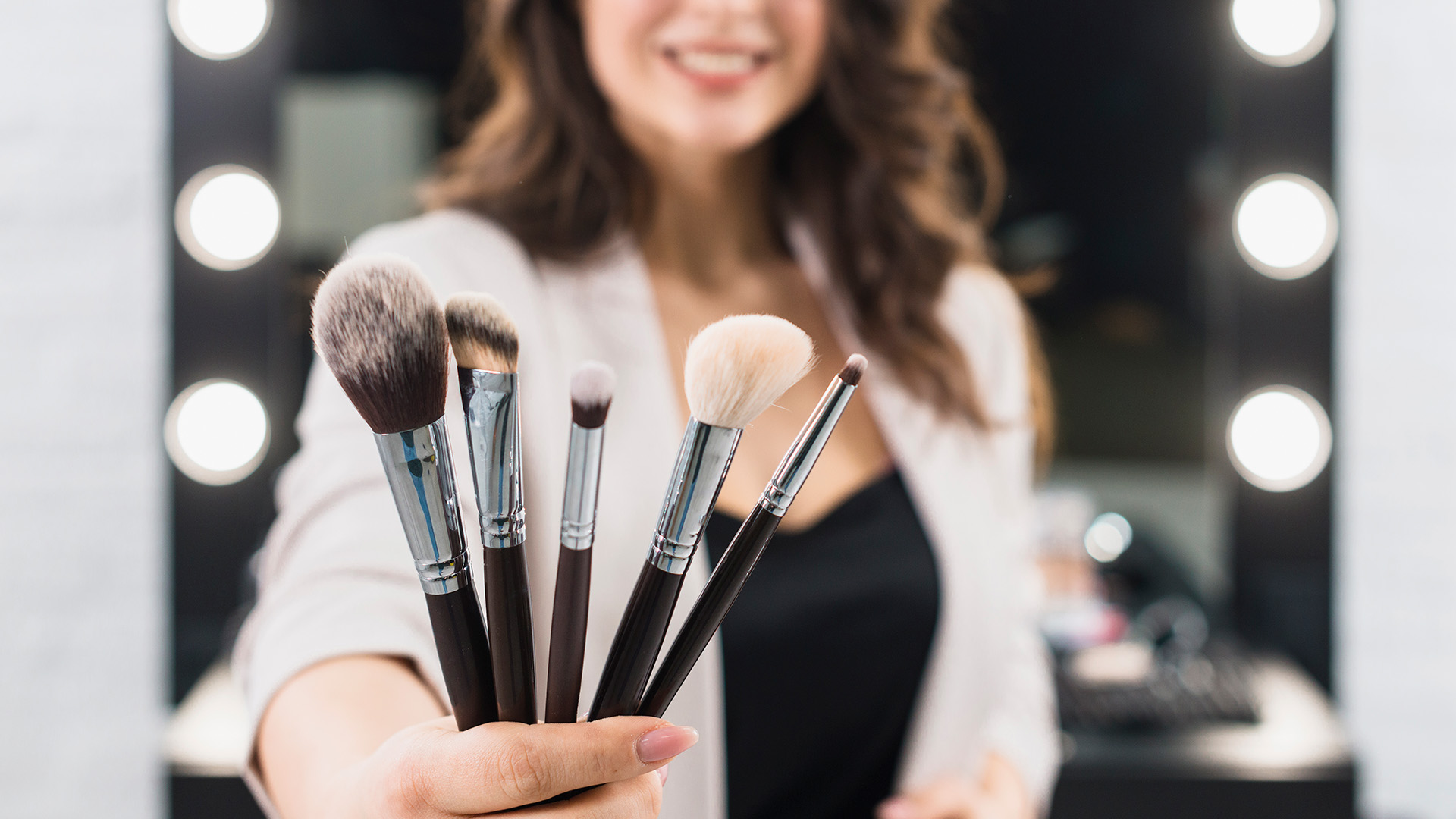 woman-showing-makeup-brushes-mirror-background