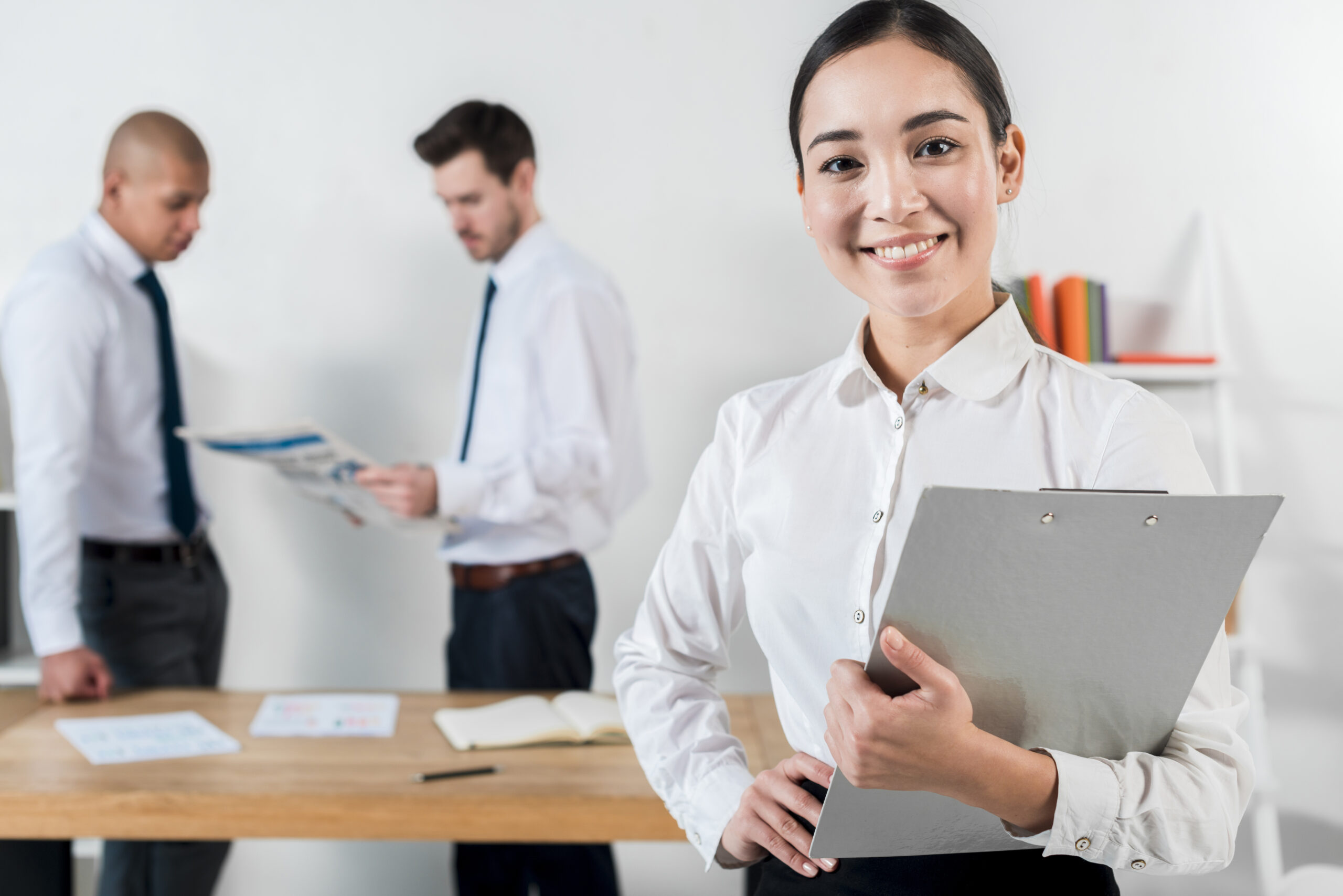 smiling-young-businesswoman-holding-clipboard-hand-with-two-businessman-working-background