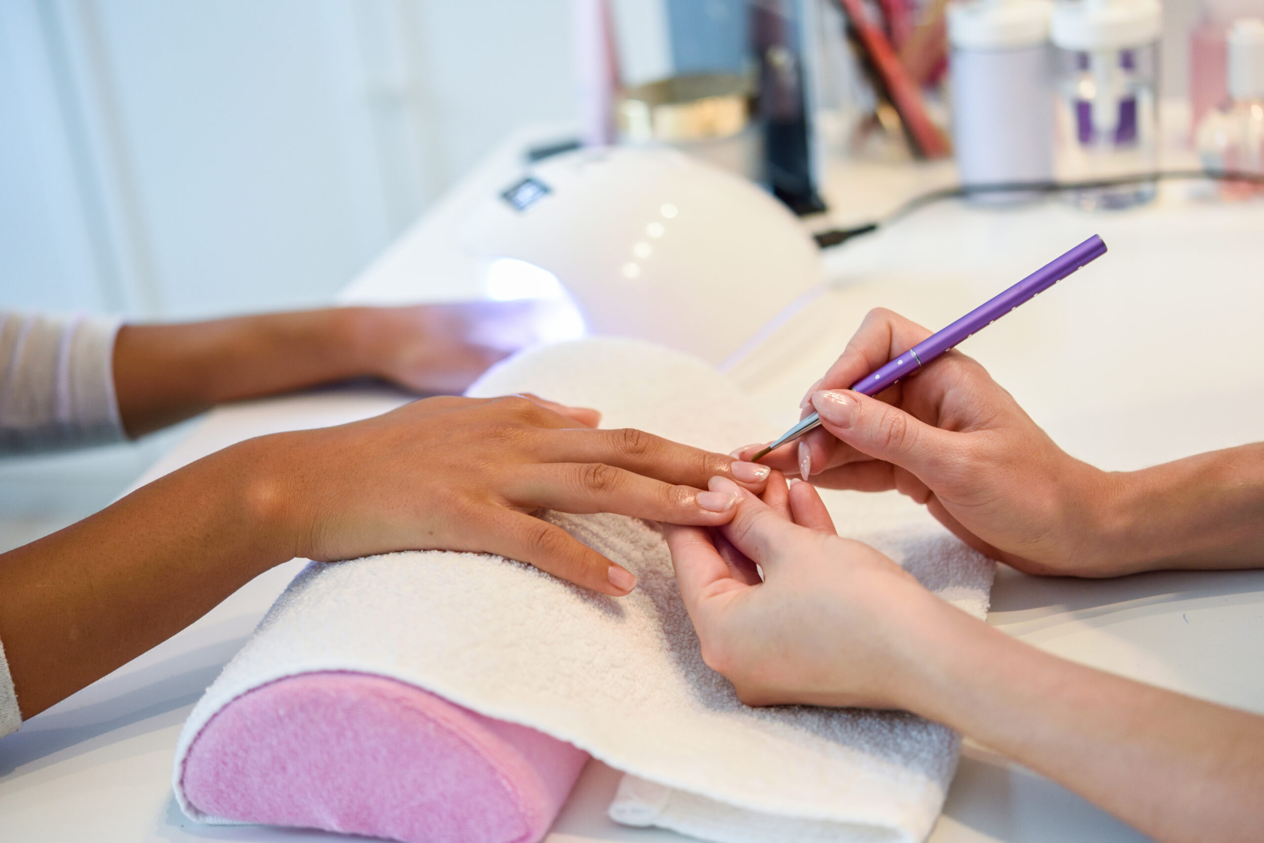 Close-up of beautician painting a woman's nails with a brush in