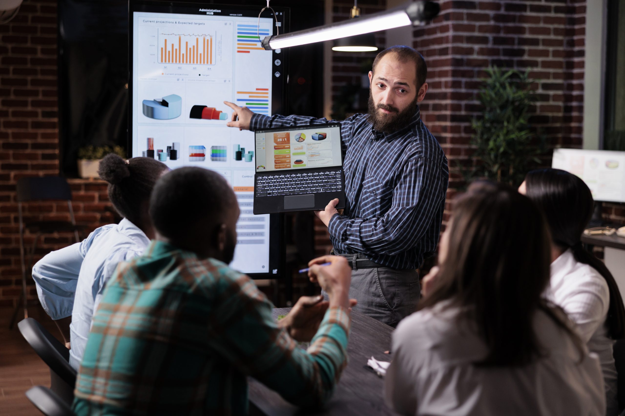 Startup entrepreneur holding laptop with sales presentation charts pointing at wall screen tv